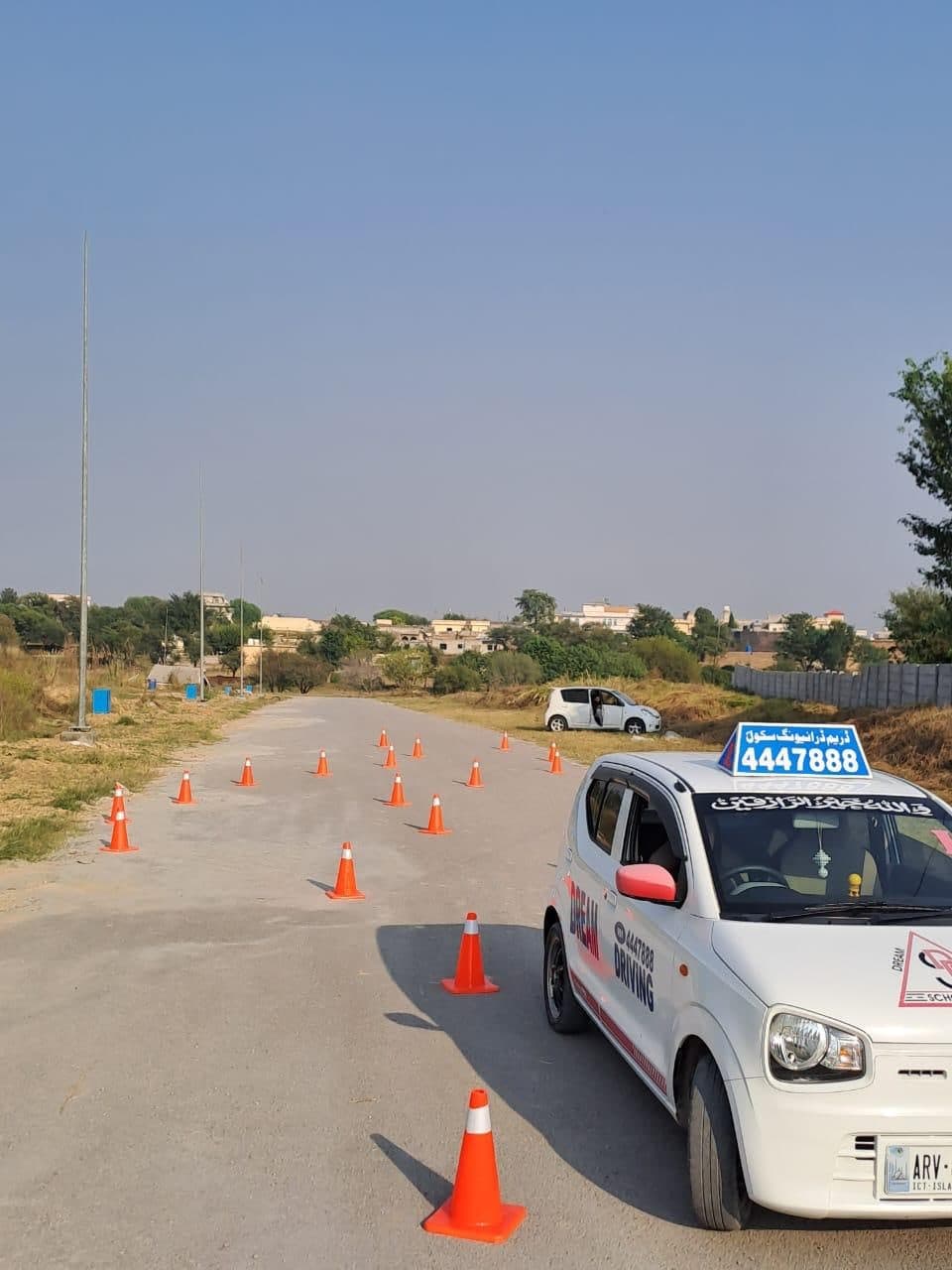 A Dream Driving School Alto on an open practice ground with a course of traffic cones laid out